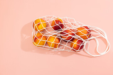 Nectarines in a white string bag on a pink background