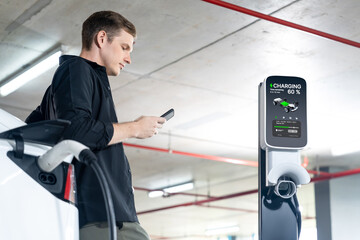 Young man travel with EV electric car to shopping center parking lot charging in downtown city...