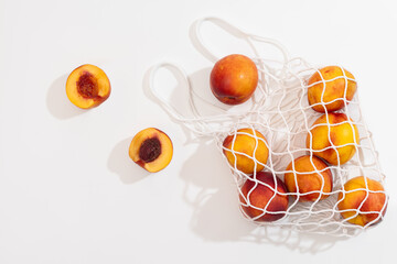 Nectarines in a white string bag on a white background