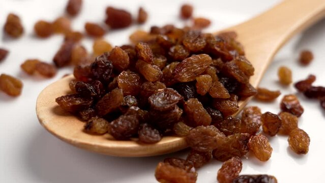 Dried brown ripe raisins in a kitchen wooden spoon on white ceramic close up. Rotation. Dry healthy fruit ingredient