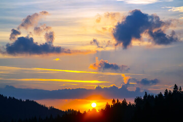 Colorful clouds in the sky at sunset against the backdrop of a mountainous forest area.