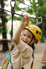 A little smiling girl climbs a rope harness in a summer  rope park pass obstacles