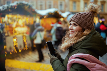 happy modern female at christmas fair in city using smartphone - obrazy, fototapety, plakaty