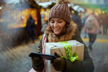 smiling modern woman at christmas fair in city using smartphone