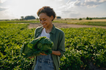 Smiling female farmer standing with just harvested cabbages on the field background