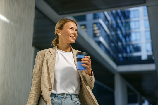 Positive female manager drinking coffee during break time near office building. High quality photo