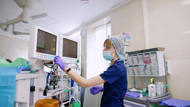 Blond female anesthesiologist setting the parameters on the lung machine monitor. Modern surgery procedure in hospital.