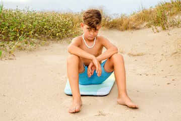 Preteen beach boy smirking cutely while sitting on his boogie board 
