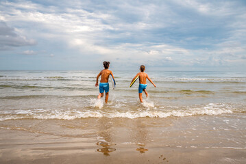 Two boys at the beach running into the water to ride their boogie boards