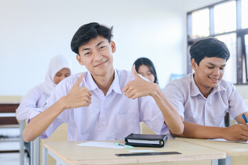 Young Asian male student showing thumbs up to the camera at the classroom