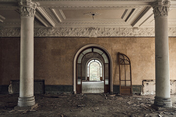 Abandoned soviet spa resort (sanatorium) Shakhter (Miner), in Tskaltubo, Georgia. View of the hall with big columns with orders. Broken arched door  © Taras Shchetinin