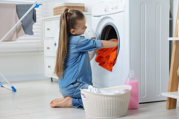 Little girl putting dirty clothes into washing machine in bathroom - obrazy, fototapety, plakaty