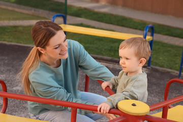 Fototapeta na wymiar Happy nanny and cute little boy on carousel outdoors