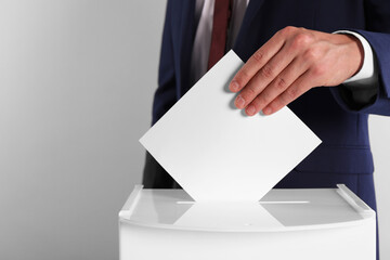 Man putting his vote into ballot box on light grey background, closeup. Space for text