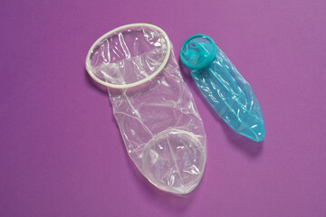 Unrolled female and male condoms on violet background, above view. Safe sex