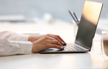 Woman using modern laptop at white desk, closeup
