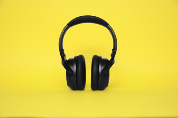 Modern black wireless headphones on yellow background