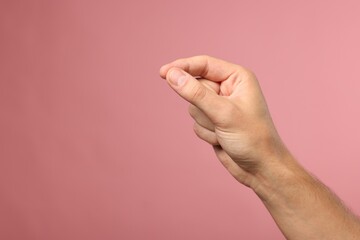Man holding something in fingers on pink background, closeup. Space for text