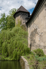 Fototapeta na wymiar Tower in park near pond. Antique aged concrete covered castle wall