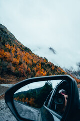 drive through a beautiful autumn landscape with mountains and trees where the reflection of the rear view mirror shows a photographer taking pictures, Araucania Andina, Araucania Region, Chile.