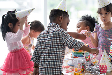 Group of multiracial little boy and girls enjoy eating beautiful rainbow cakes and candy in party
