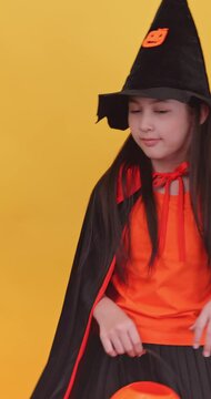 Vertical clip. Cute little girl wearing a witch costume to celebrate Halloween on yellow background.