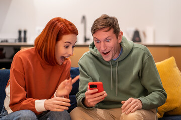 Amazed shocked happy man woman rejoicing looking at smartphone screen at home. Winning the lottery,...