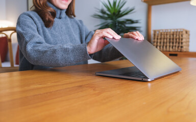 Closeup image of a woman closing or opening a laptop computer on table after finished using it