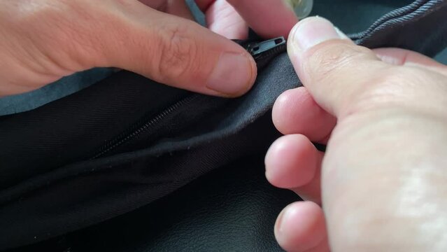 Hand sliding broken zipper on black pants close up view. Clothing fix and repair concept