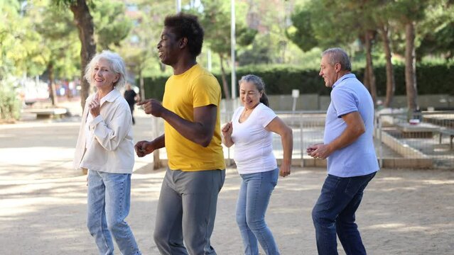  Group of happy women and men different ages practicing Cha-cha-cha in a summer park