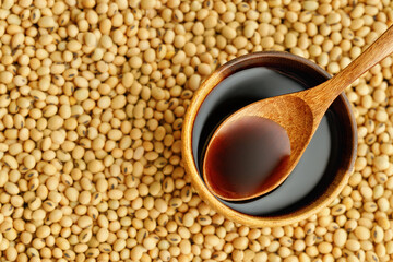top view of soy sauce in bowl and in spoon on dry soybeans as background