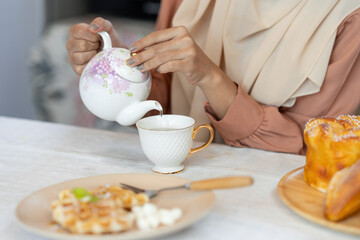 young muslim woman in hijab eating sweets, bread, waffles, cakes, healthy food menu and happily drinking hot tea for breakfast in the kitchen at home Holiday concept, lifestyle