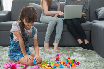 child a little girl is playing blocks at home. Mother with friend working on laptop or shopping online