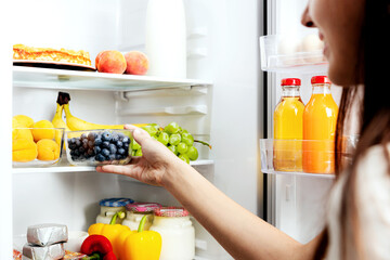 Woman hand taking, grabbing or picks up box of blueberry out of open refrigerator shelf or fridge...