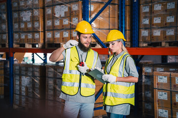 Warehouse worker logistic team wearing hard hat working in aisle between tall racks with packed goods warehouse for industry business of import, export delivery to global market, shipping management