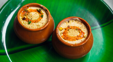 Kulfi or Qulfi ice cream in a clay pot. Kulfi is a popular traditional Indian dessert made of milk with spices and nuts. Two clay pots with ice cream on a green plate in the form of a leaf - obrazy, fototapety, plakaty