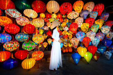 Tourists in traditional Vietnamese clothing look at paper lanterns in Hoi An ancient town....