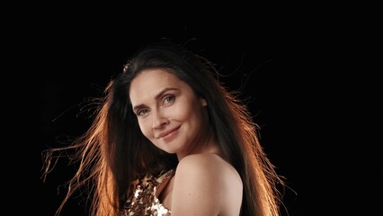 A middle-aged woman. Standing sideways and looking at the camera slightly and smiling, the light...