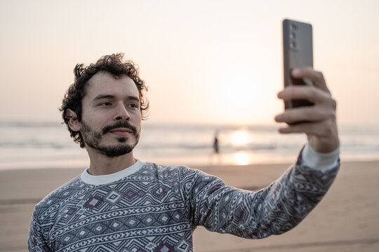 Young man takes a selfie photo on the beach at sunset