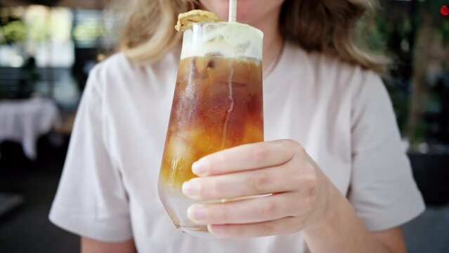 Close view of a woman holding and drinking a cold brew espresso shot drink with matcha foam and straw in a cafe