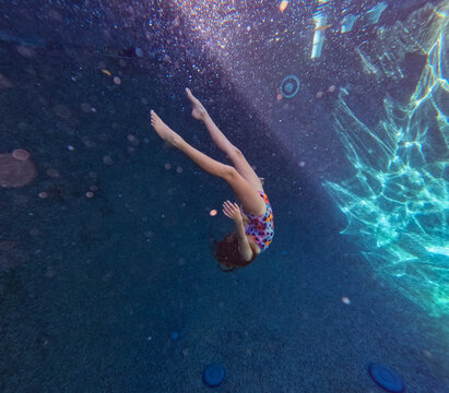 Girl swimming deep in a blue underwater pool with sunshine bokeh