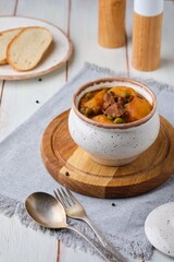 Hearty Irish stew of beef, potatoes and green peas in beer sauce in a ceramic pot on a light wooden background. Irish cuisine.