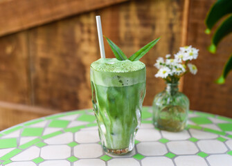 blended brew matcha latte with straw on green table and wooden wall