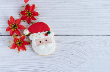 Biscuit with Santa's face on a white wooden background with red flowers decoration.
