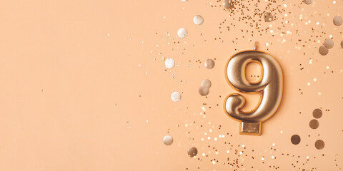 Gold candle in the form of number nine on peach background with confetti. - obrazy, fototapety, plakaty
