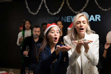 New Year party, Group of young people in Santa hats blowing confetti while celebrating new year