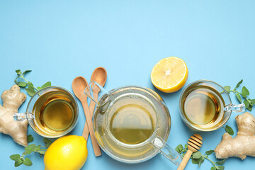 Cups and teapot with tea, lemon, ginger on blue background, space for text