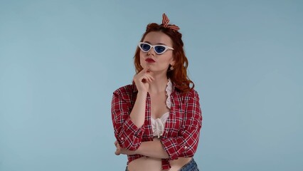 In the frame is a young woman on a blue background. Looking into the distance wearing sunglasses. Thinking about something, thinking, dreaming, fantasizing. Supporting her head with her hand HDR