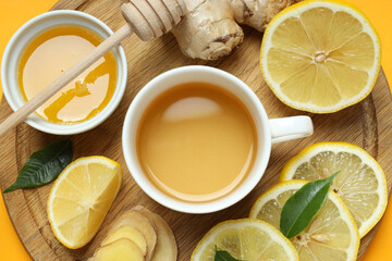 Cup with tea, lemon, ginger and honey on yellow background, top view