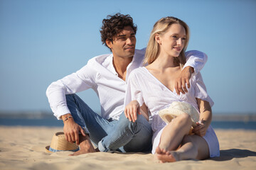 happy young couple sitting on sandy beach